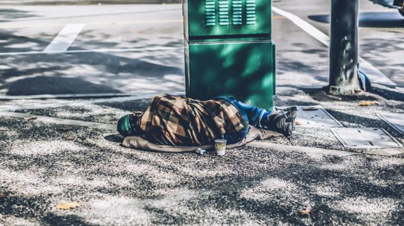 Photo of homeless man sleeping on street corner