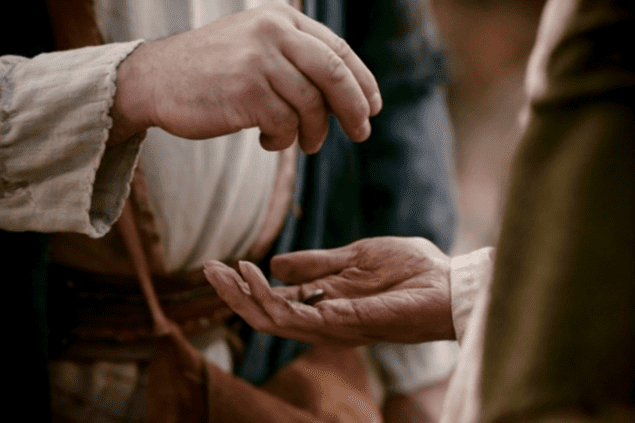 Closeup photo of biblical man dropping coins in another man's hands