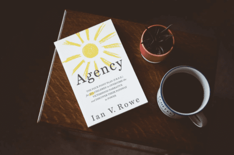 Book "Agency" by Ian V. Rowe sitting on table with coffee and plant
