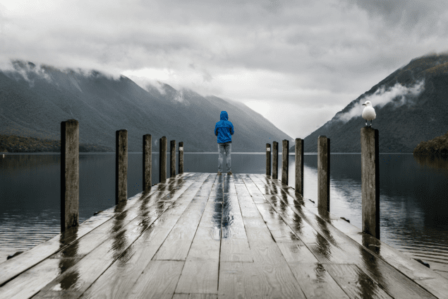Photo of person standing at edge of dock with large lake and mountains in background