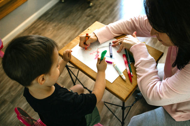 Photo of child and daycare ministry worker drawing with crayons together.