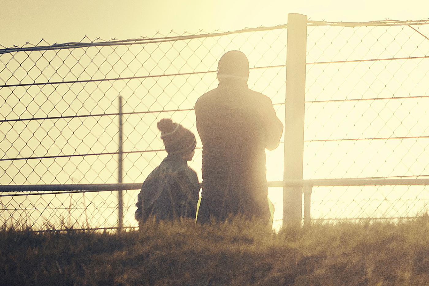 Photo of man and boy standing behind chain link fence